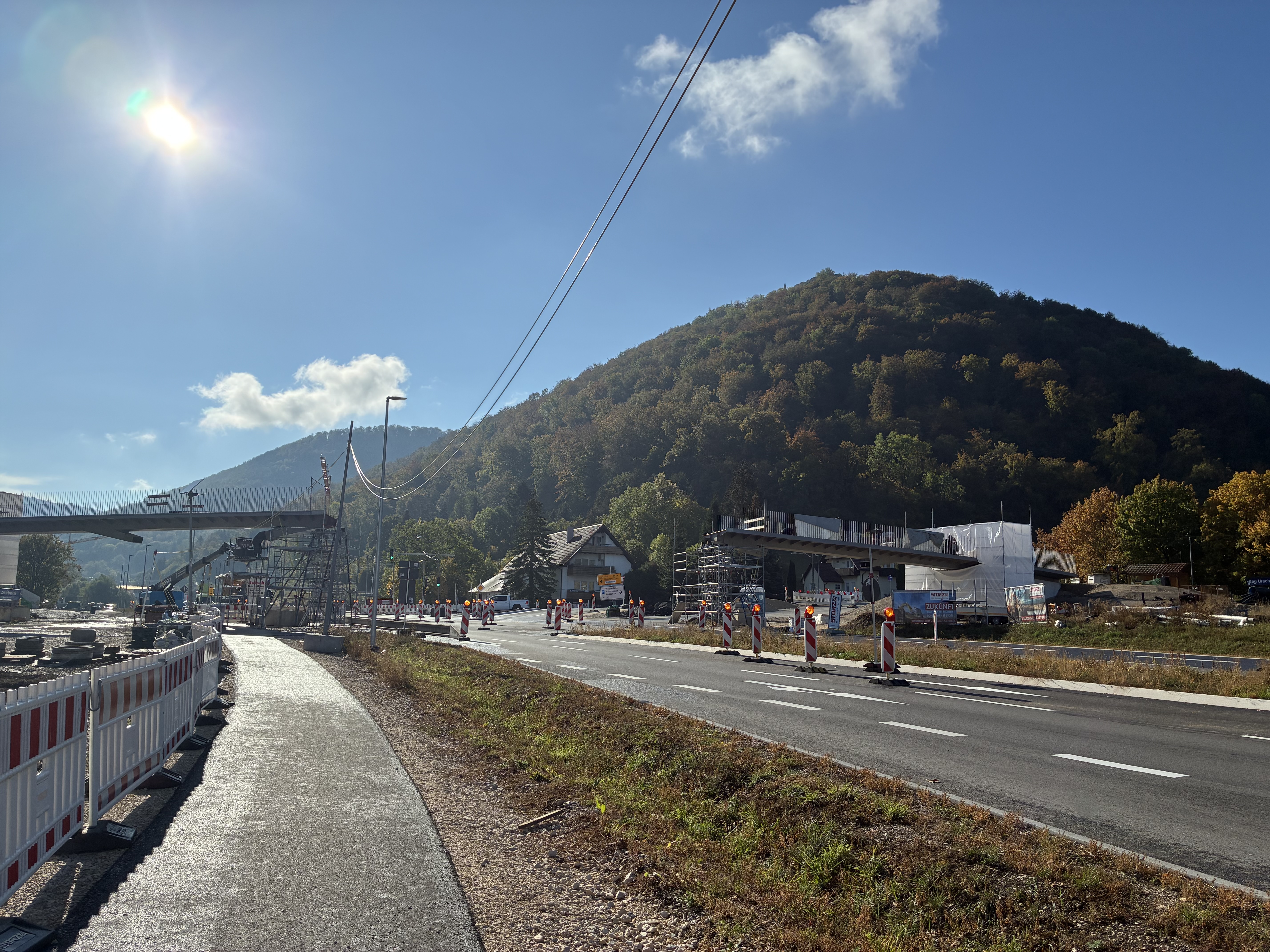 Das Foto zeigt die B 28. Daneben einen frisch asphaltieren Radweg. Im Hintergrund sieht man die im Bau befindliche Fuß- und Radwegbrücke in Bad Urach