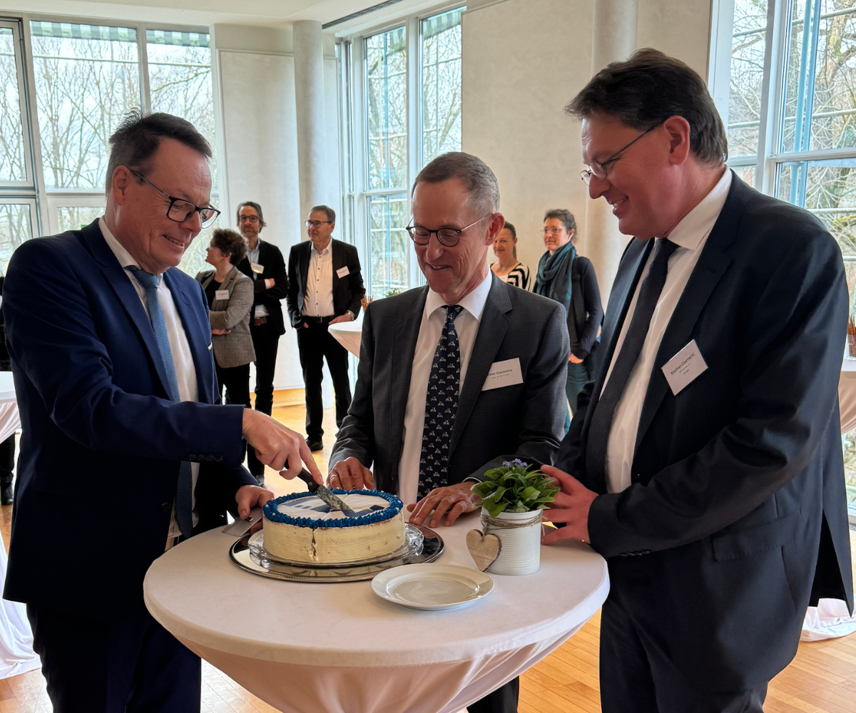 Das Foto zeigt Regierungspräsident Klaus Tappeser, den früheren Abteilungsleiter Peter Goossens und den aktuellen Leiter der Abteilung Marktüberwachung, Stephan Czarnecki an einem Stehtisch beim Kuchenanschnitt