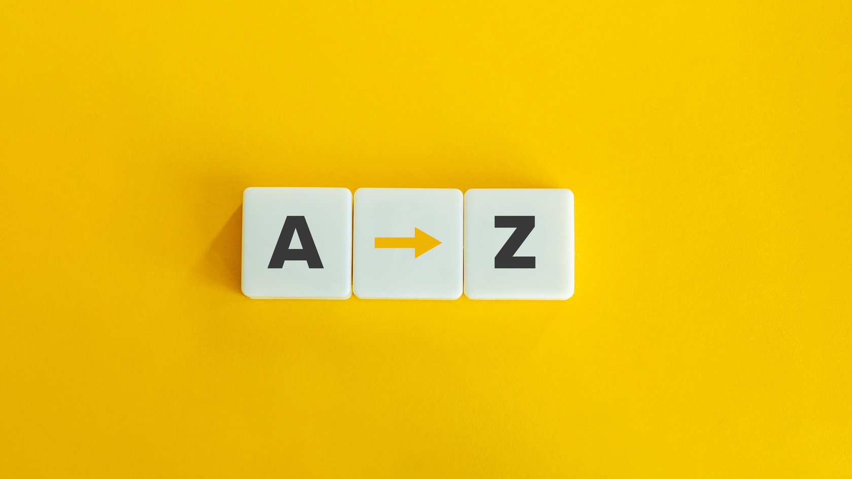 Zwei Scrabbelbuchstaben, A und Z, auf gelbem Untergrund. zwischen den Buchstaben liegt ein Pfeil.