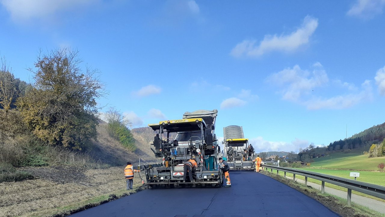 Man sieht Baustellenfahrzeug das neuen Asphalt auf einer Straße walzt