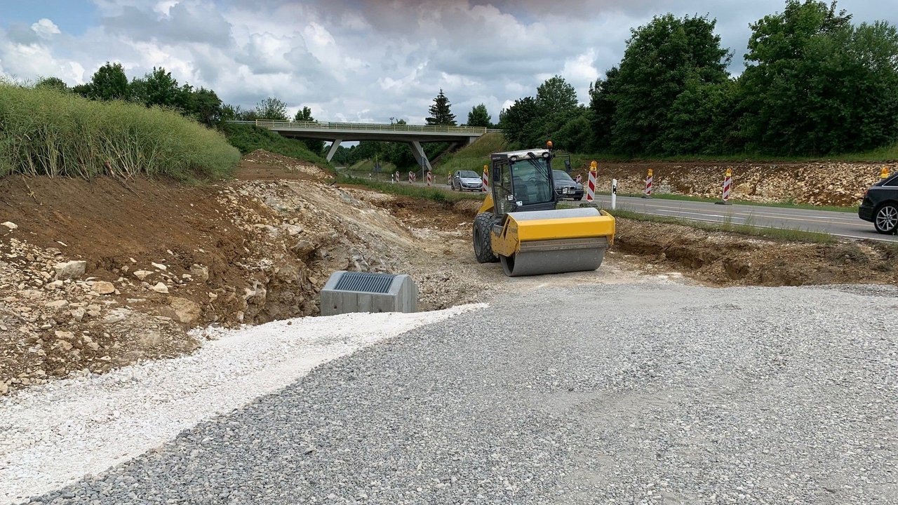 Das Foto zeigt ein geschottertes Stück neben der L 1230 und eine Baustellenwalze. Im Hintergrund eine Brücke