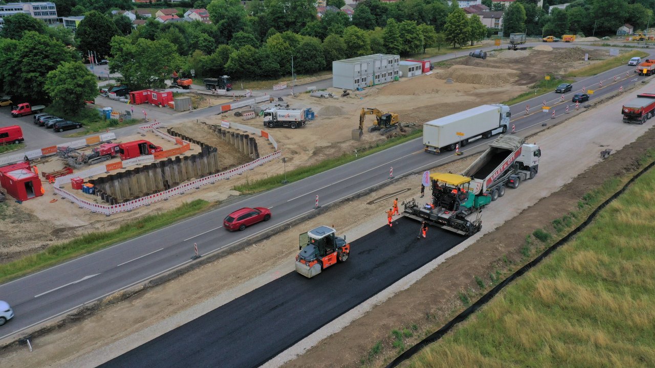 Das Foto zeigt die Baustellenarbeiten auf der B 28 Behelfsfahrbahn am Knotenpunkt Wasserfall. Mehrere Baustellenfahrzeuge beim Asphaltieren der Fahrbahn.