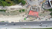 Luftbild eines Flusses. An beiden Ufern werden große Blöcke betoniert, zwischen diesen Blöcken befindet sich eine Plattform, die den ganzen FLuss überspannt.