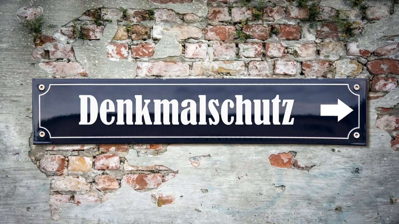 Das Foto zeigt die eine Mauer an der ein Schild befestigt ist mit dem Schriftzug "Denkmalschutz"