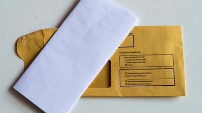 Ein gefalteter Briefbogen liegt auf einem Kuvert, auf dem Persönliche Zustellung steht.