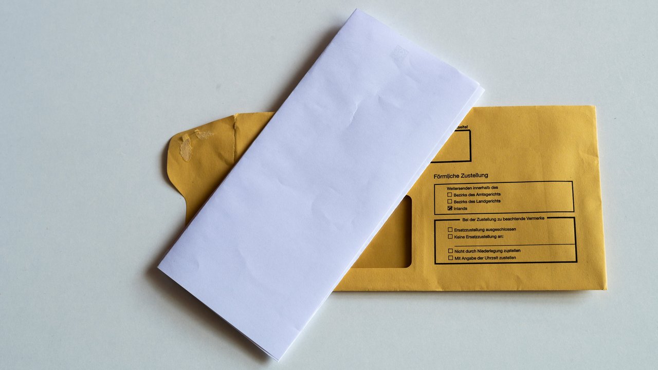 Ein gefalteter Briefbogen liegt auf einem Kuvert, auf dem Persönliche Zustellung steht.