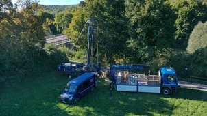 Luftbild: Bohrgerät und Fahrzeuge stehen neben einer Brücke