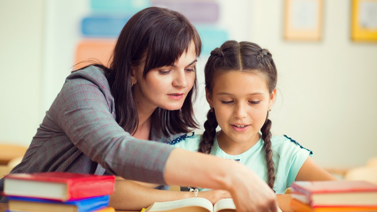 Junge Lehrerin mit Schülerin Junge Lehrerin mit Schülerin an einem Schreibtisch mit vielen Büchern darauf