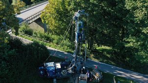 Luftbild: Bohrgerät und Fahrzeuge stehen neben einer Brücke