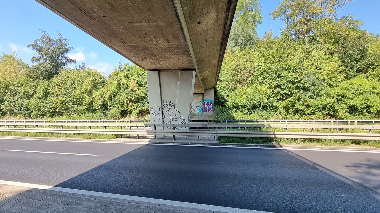 Das Foto zeigt eine Feldwegbrücke von unten, die über eine Straße führt.