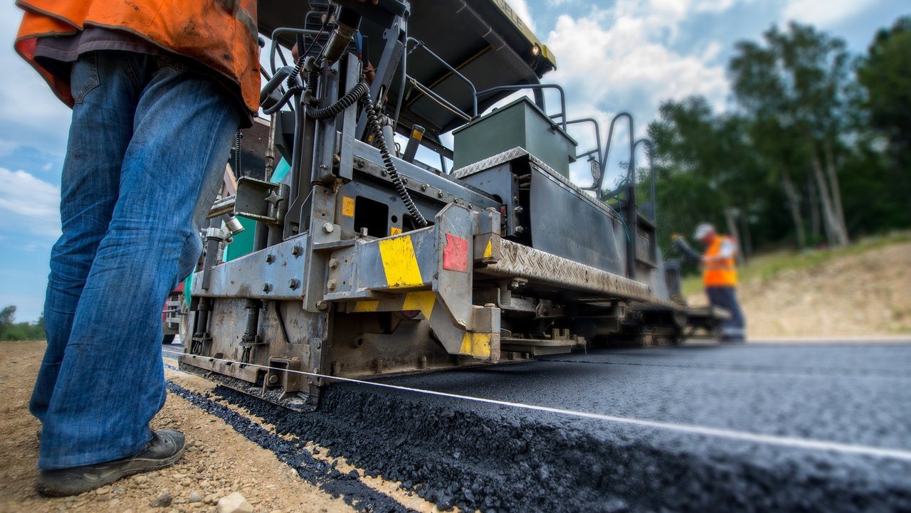 Man sieht die Konstruktion einer neuen Straße; Ein Straßenbaufahrzeug fährt über frischen Asphalt