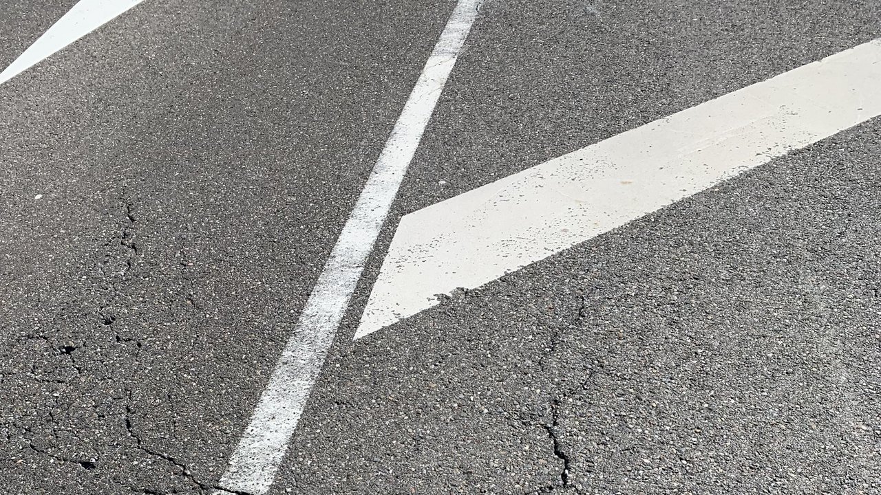 Das Bild zeigt eine beschädigte Straße mit Rissen und weißer Markierung