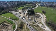 Ein Luftbild einer Baustelle, im Hintergrund der Bodensee. Auf der Baustelle sind zwei große Betonwände sichtbar, zischen denen Kräne ein Stahlgerüst aufbauen.