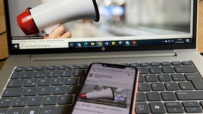 Symbolbild Bekanntmachungen: Ein Handy liegt auf einem Laptop und zeigt die Bekanntmachungsseite des Regierungspräsidiums Tübingen, ebenso ist diese Seite auf dem Monitor zu sehen