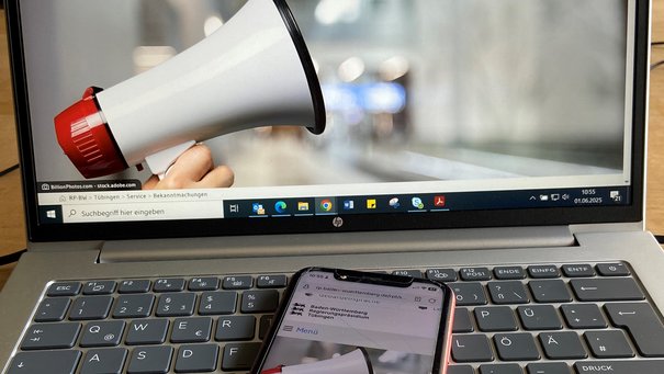 Symbolbild Bekanntmachungen: Ein Handy liegt auf einem Laptop und zeigt die Bekanntmachungsseite des Regierungspräsidiums Tübingen, ebenso ist diese Seite auf dem Monitor zu sehen
