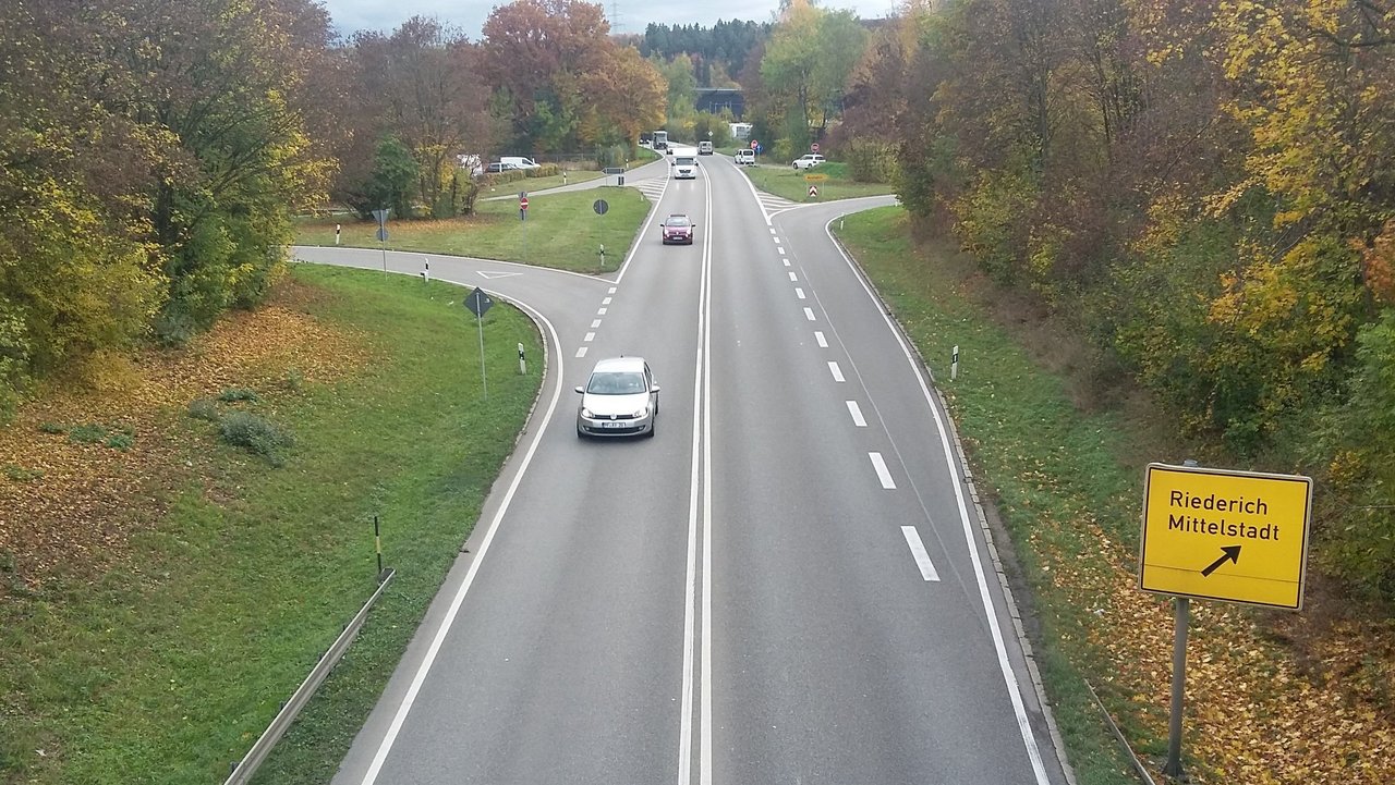 Man blickt von oben auf die B 312 Anschlussstelle L 374 bei Riederich; mehrere Fahrzeuge sind zu sehen; Straßenmarkierungen und ein Straßenschild