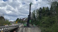 Ein Bohrgerät steht neben einer Brücke. Neben der Maschine sind Arbeiter zu sehen. 
