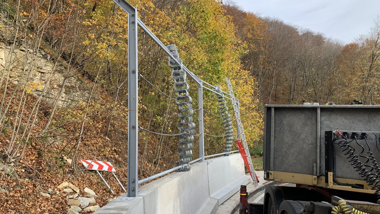 Das Foto zeigt Fangzäunen aus hochfestem Drahtgeflecht an einem Hang, welche zur Felssicherung auf Betonteile aufgesetzt sind.