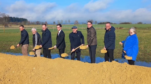 Acht Personen stehen mit Spaten vor einem kleinen Erdwall.