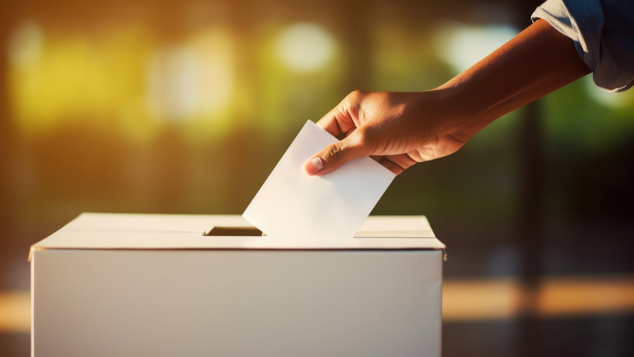 Das Foto zeigt eine Hand, die einen Wahlzettel in den Schlitz einer Wahlurne gibt