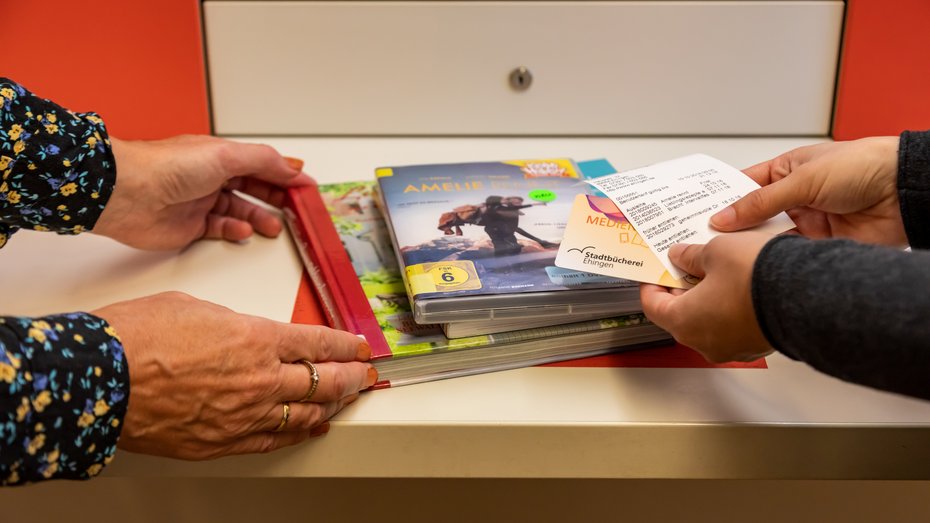 Stadtbücherei Ehingen an der Donau - Verbuchung Vier Hände halten CDs und Bücher an den Selbstverbucher der Stadtbücherei Ehingen an der Donau