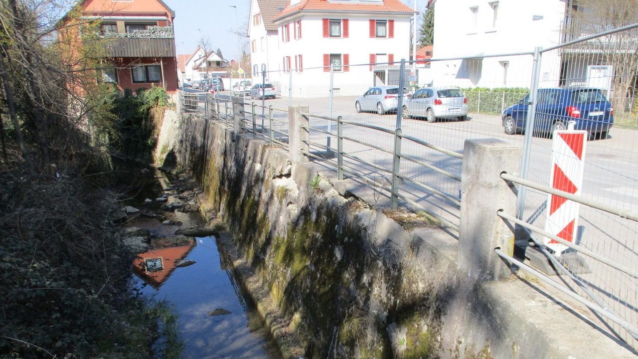 Das Bild zeigt die Stützwand entlang der L 382 und den Gewässerlauf am Eierbach in Pfullingen; man sieht Häuser und parkende Autos entlang der Friedrichstraße