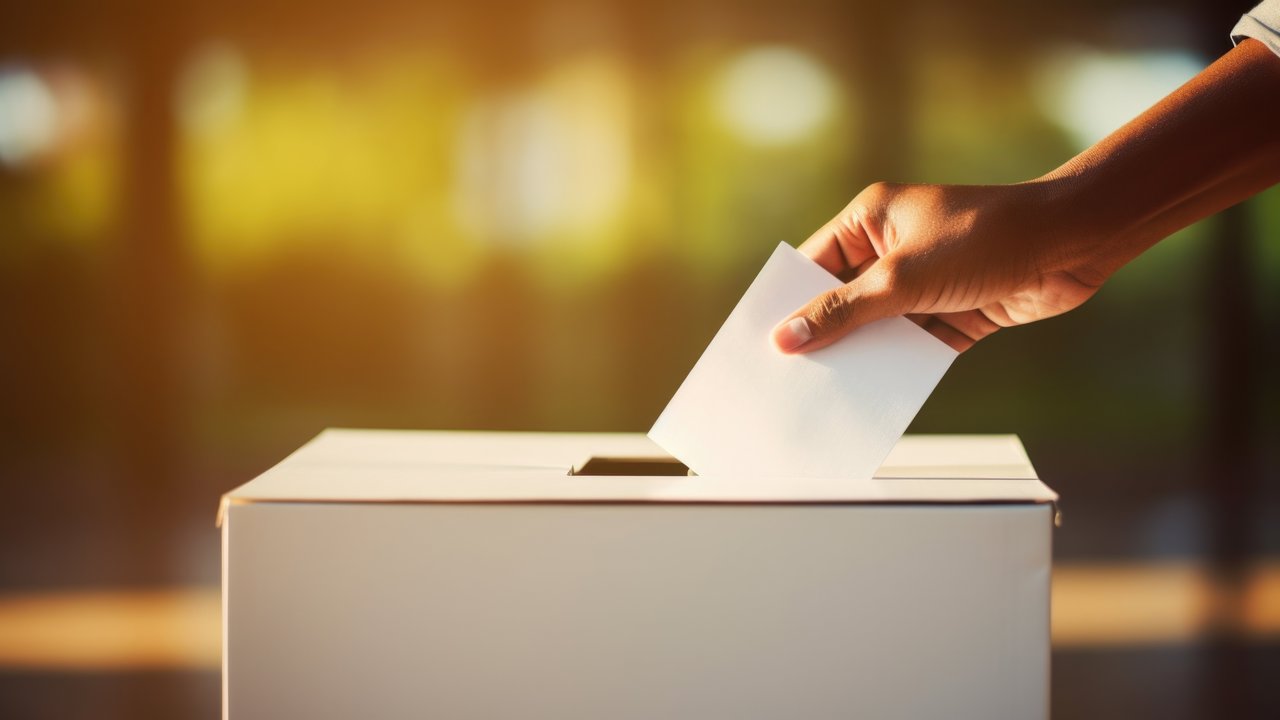 Das Foto zeigt eine Hand, die einen Wahlzettel in den Schlitz einer Wahlurne gibt