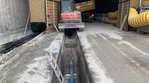 Eine Straße, in die ein Graben gefräst wurde. In dem Graben verläuft ein blaues Rohr. Im Hintergrund ist ein Tunneleingang erkennbar.