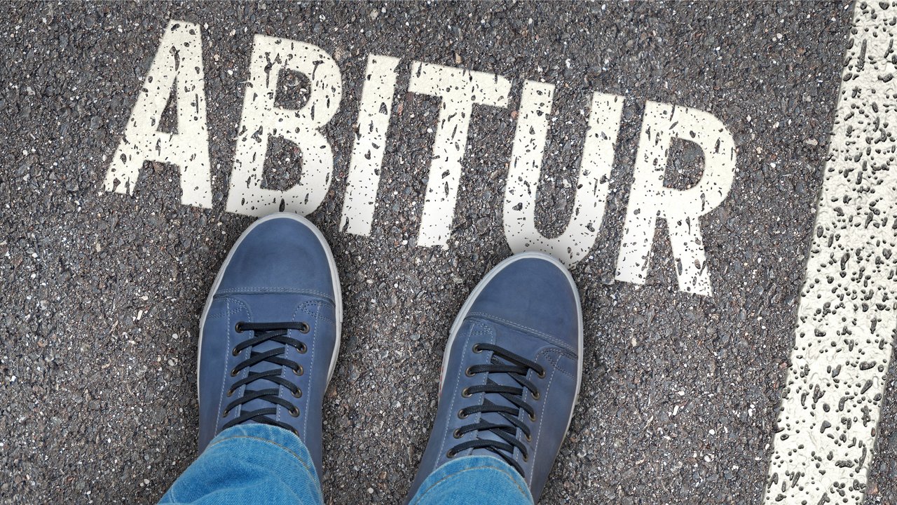 Das Foto zeigt die Schuhe einer Person auf einer Straße mit dem Schriftzug "Abitur"