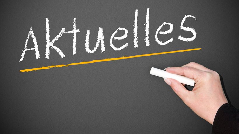 Eine Hand schreibt mit weißer Kreide "Aktuelles" auf eine Schultafel