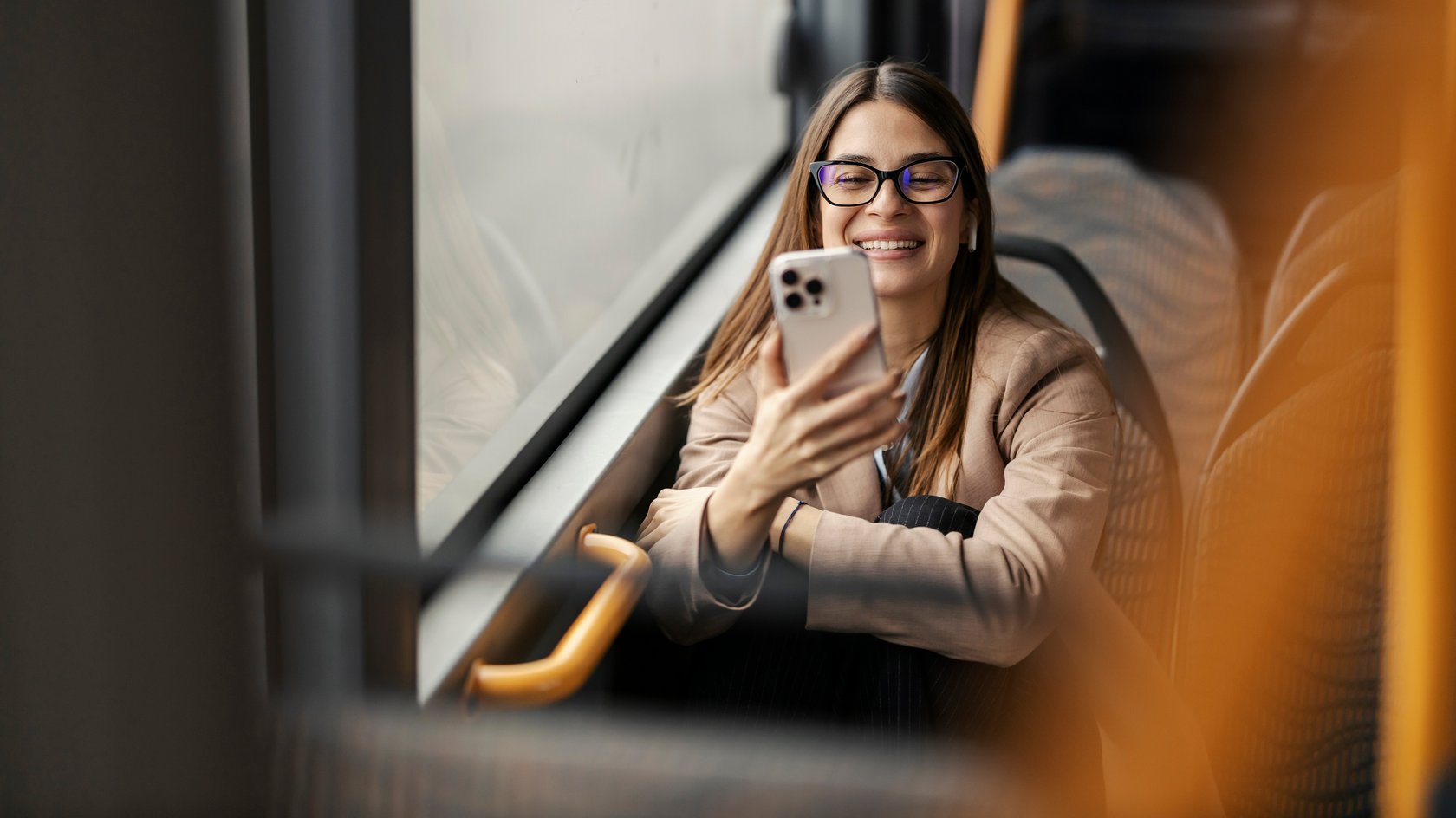 Eine junge Frau sitzt im Bud und blickt lächelnd auf ihr Handy.