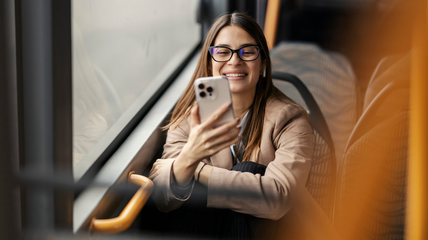 Eine junge Frau sitzt im Bud und blickt lächelnd auf ihr Handy.