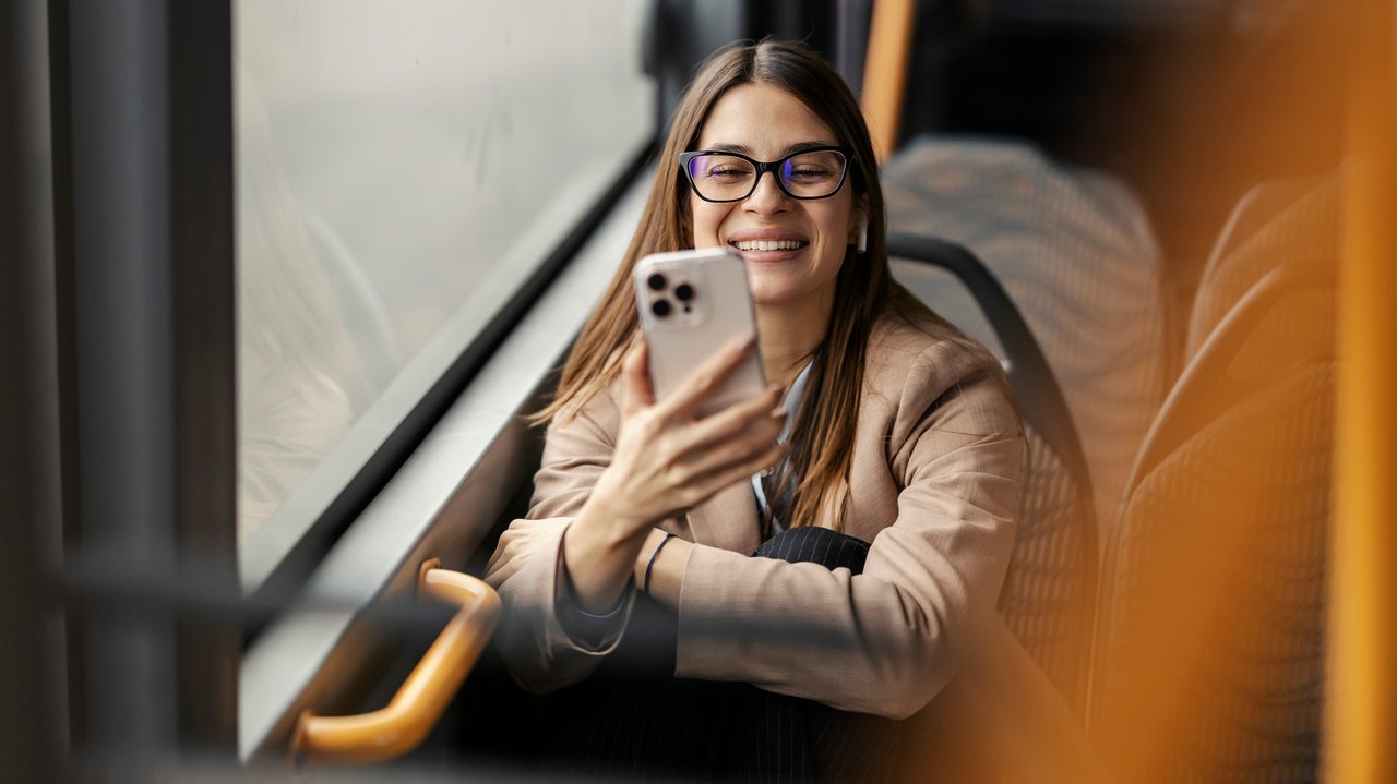 Symbolbild Barrierefreiheit Eine junge Frau sitzt im Bud und blickt lächelnd auf ihr Handy.