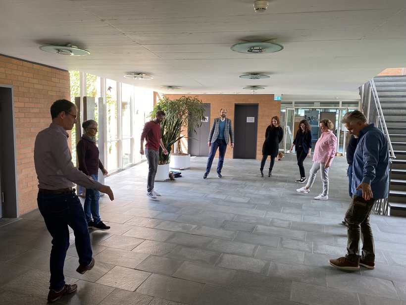 Eine Gruppe Menschen steht in einem Foyer im Kreis und macht Gymnastik