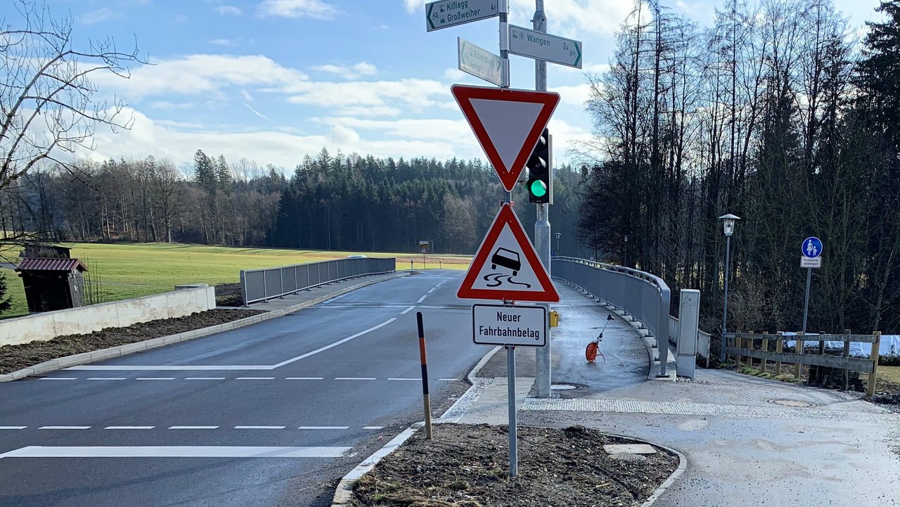 Das Foto zeigt den Ersatzneubau der Brücke Herfatz. Eine Ampelanlage. Straßen- und Radwegschilder. Im Hintergrund Wiesen und Wälder