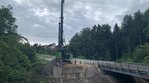 Juli 2025: Die Bohrpfähle für die Widerlager der neuen Brücke werden hergestellt. Ein Bohrgerät neben einer Brücke