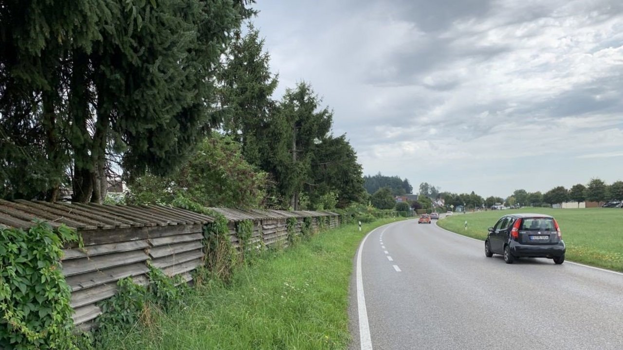 Das Foto zeigt eine Straße, auf der mehrere Autos fahren; links sieht man eine Lärmschutzwand und ein Waldstück