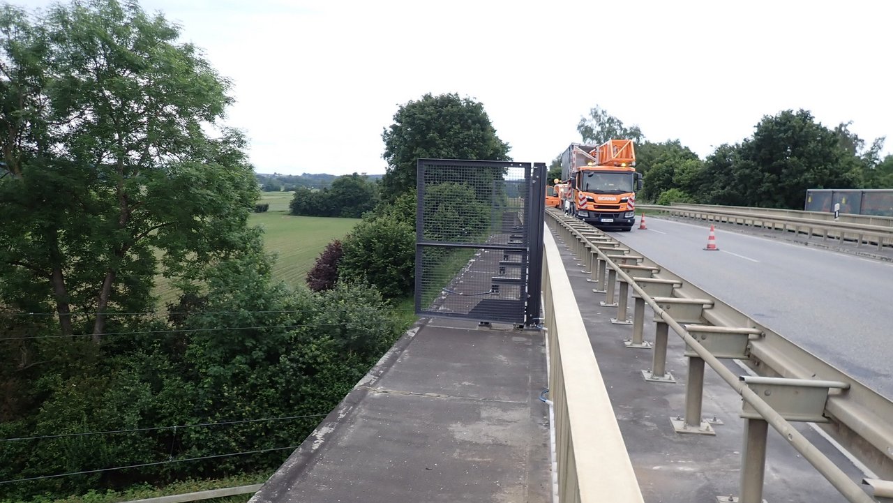 Das Foto zeigt Instandsetzungsarbeiten mit einem Baustellenfahrzeug auf einer Brücke die über Bahngleise führt