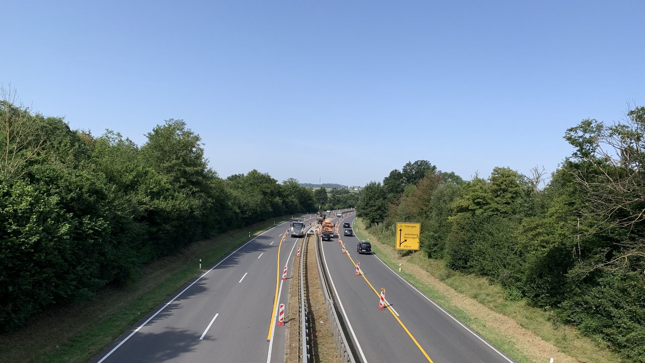 Das Foto zeigt die B 28 zwischen Tübingen und Reutlingen. Auf der Fahrbahn ist eine Umleitespur gelb eingezeichnet. In der Mitte eine begrünte Mittel-Leitplanke. Rechts- und Links Büsche und Bäume