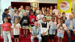 Gruppenfoto bei der Auftaktveranstaltung HEISS AUF LESEN© 2025. Mehrere Kinder und vorne in der Mitte Herr Boris Palmer (Oberbürgermeister der Stadt Tübingen) sowie vorne rechts Herr Oliver Steller (Künstler)