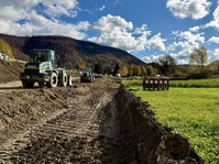 Ein Radlader auf einer Erdpiste neben einer Straße. Die Erde wird zu einem Damm aufgeschüttet. 