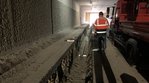 In einem Tunnel läuft ein Graben, in dem eine Röhre liegt. Neben dem Graben steht ein Mann in einer orangenen Bau-Jacke.