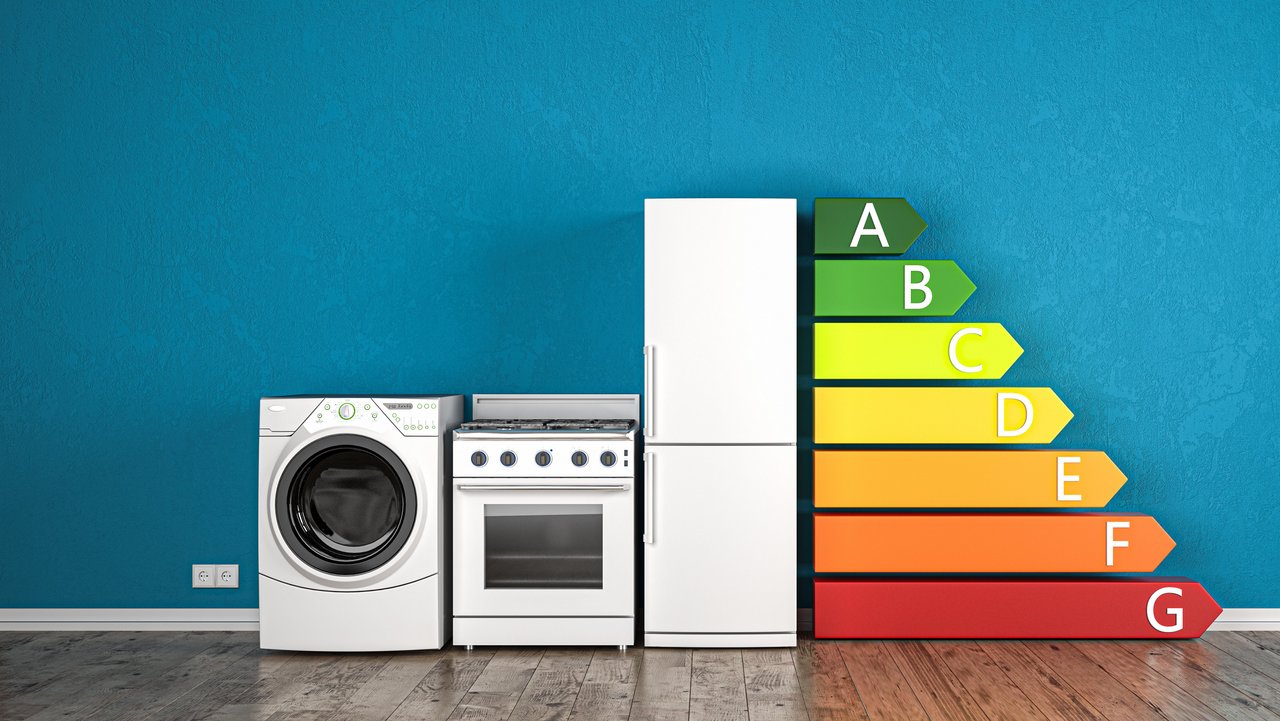 Von links nach rechts werden eine Waschmaschine, ein E-Herd, ein Kühlschrank gezeigt. Daneben werden rechts in den Farben von Grün über Gelb nach Rot die Energieeffizienzklassen von A bis G abgebildet