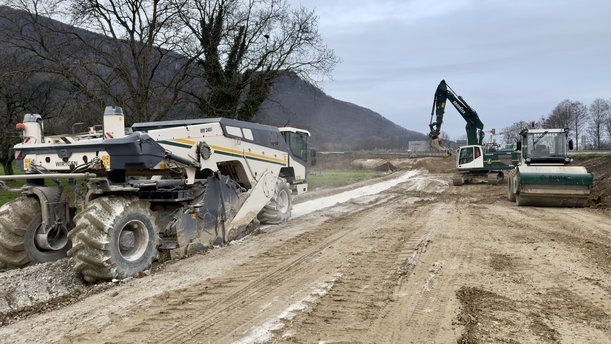 Eine Baumaschine steht auf einer planierten Erdpiste. 