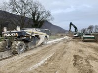 Eine Baumaschine steht auf einer planierten Erdpiste. 