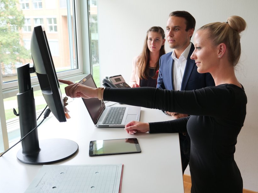 Kolleginnen und Kollegen blicken auf den PC-Bildschirm und diskutieren.