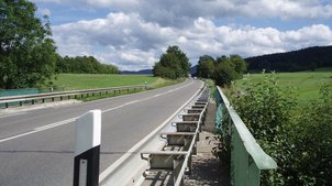 Eine Straße neben einer Wiese, im Hintergrund Wald