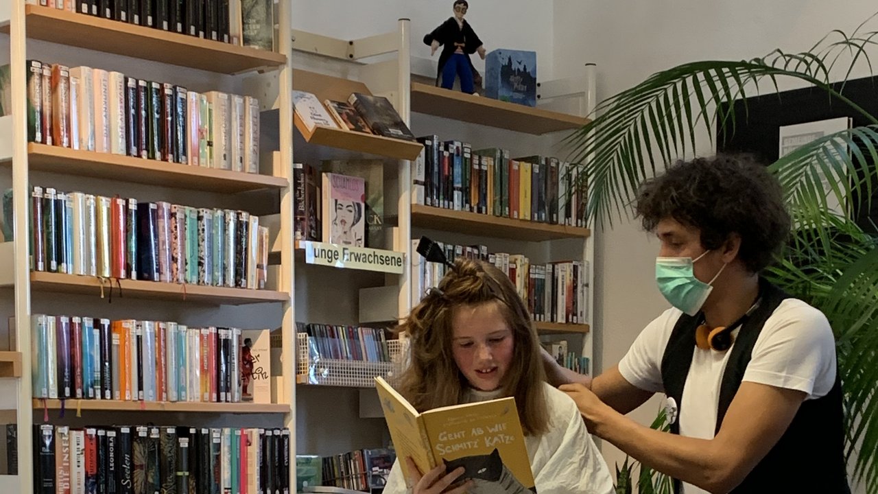 Ein Friseur schneidet einem Mädchen in einer Stadtbibliothek die Haare