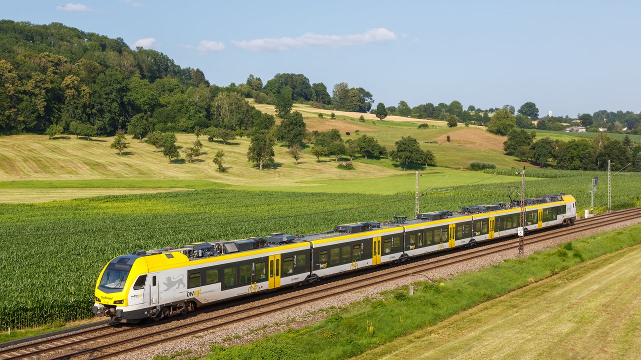 Das Bild zeigt einen gelben Regionalzug der durch ein Tal fährt
