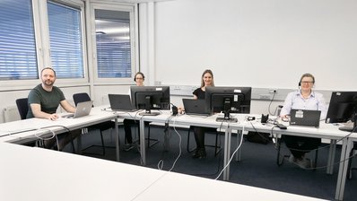 Kolleginnen und Kollege der Servicestelle Stoffliche Marktüberwachung sitzen zusammen in einem Besprechungsraum mit ihren Laptops